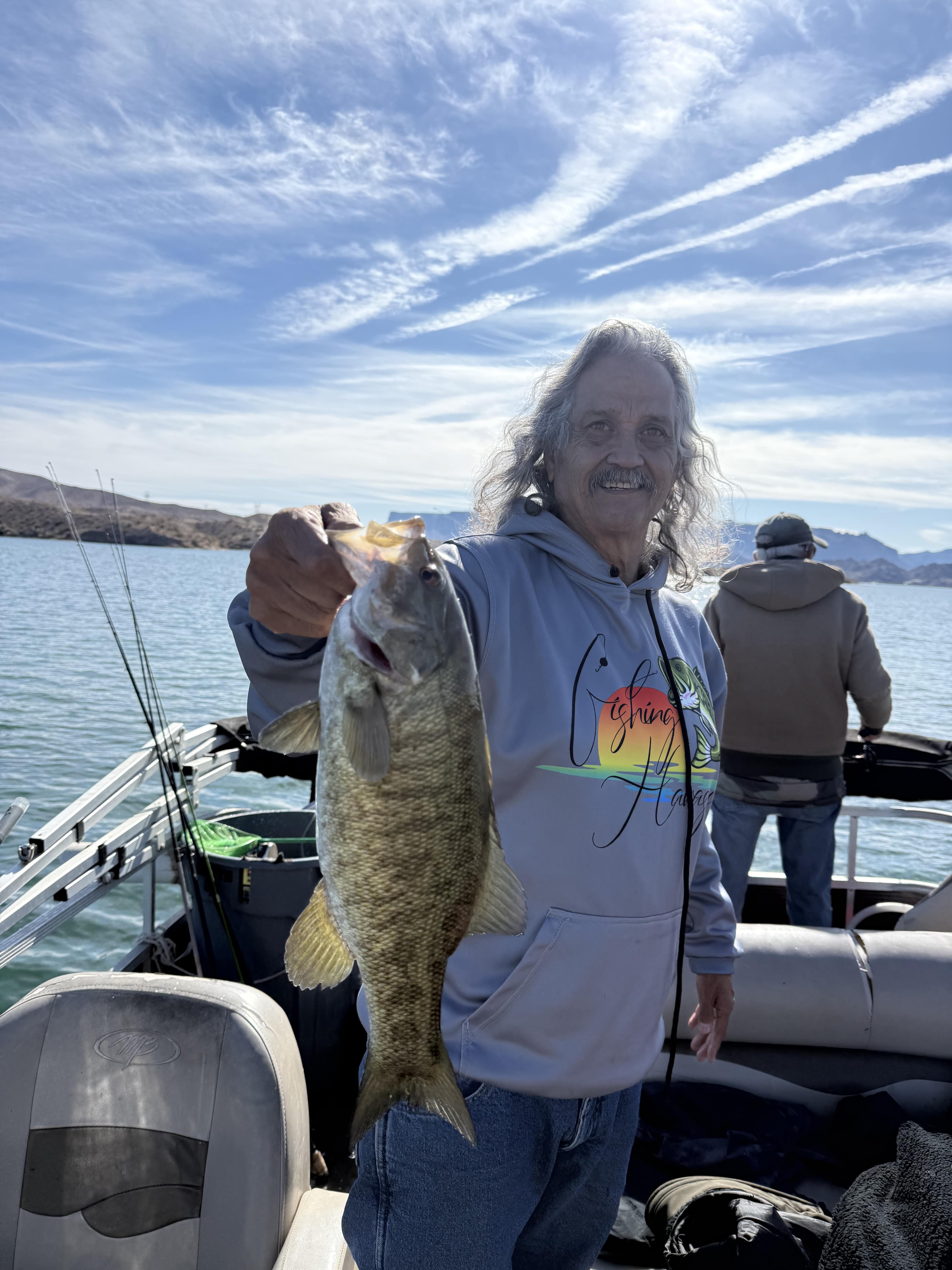 Angler holding a bass in front of rocky shoreline